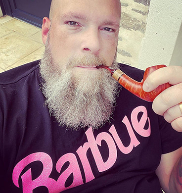 Un homme barbu avec un t-shirt Barbue qui fume la pipe